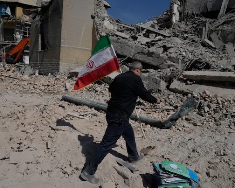 A man carries an Iranian flag to place on the rubble of a police facility struck during the U.S.–Israeli military campaign in Tehran, Iran, Wednesday, March 4, 2026. (AP Photo/Vahid Salemi)