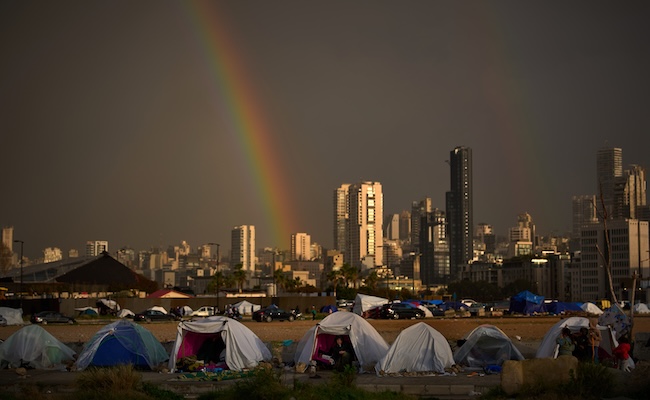 Displaced people who fled Israeli strikes in southern Lebanon sit inside tents used as shelters as a rainbow breaks through the rain in Beirut, Lebanon, Sunday, March 29, 2026. (AP Photo/Emilio Morenatti)