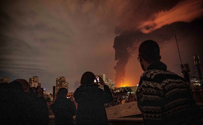 Residents look on and take pictures as flames and smoke rise from an oil storage facility struck as attacks hit the city during the US-Israeli military campaign in Tehran, Iran, Saturday, March 7, 2026. (Alireza Sotakbar/ISNA via AP)