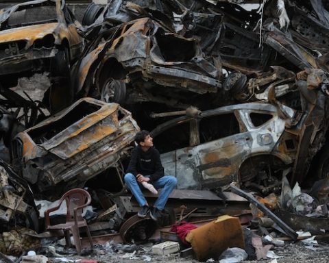 A man sits next to charred cars and wreckage where a building was destroyed by an Israeli airstrike the previous Wednesday, in central Beirut, Lebanon, Tuesday, April 14, 2026. (AP Photo/Hassan Ammar)