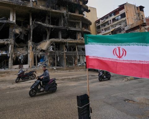 A man on his scooter passes next to an Iranian flag placed in front of a destroyed building, following a ceasefire between Hezbollah and Israel, in Dahiyeh, Beirut's southern suburbs, Lebanon, Monday, April 20, 2026. (AP Photo/Hussein Malla)