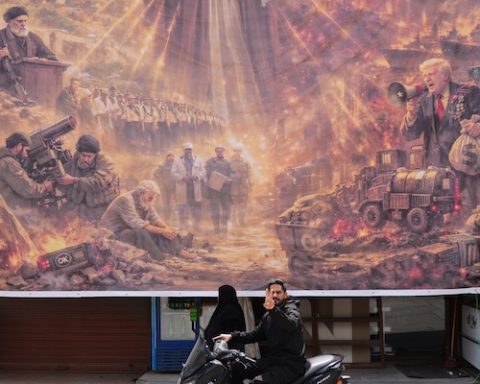 A man on a scooter flashes a victory sign as he drives past a giant portrait depicting the war in the Middle East triggered by the U.S.-Israel strikes on Iran on Feb. 28, in the southern village of Kfar Sir, Lebanon, on Tuesday, April 21, 2026. (AP Photo/Hassan Ammar)