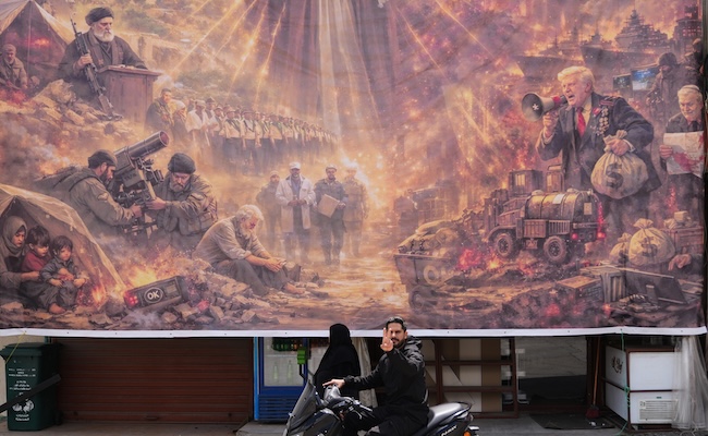 A man on a scooter flashes a victory sign as he drives past a giant portrait depicting the war in the Middle East triggered by the U.S.-Israel strikes on Iran on Feb. 28, in the southern village of Kfar Sir, Lebanon, on Tuesday, April 21, 2026. (AP Photo/Hassan Ammar)