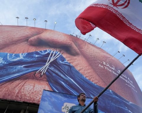A man waves an Iranian flag for a pro-government campaign under a billboard with graphic showing Strait of Hormuz and sewn lips of U.S. President Donald Trump in a square in downtown Tehran, Iran, Wednesday, May 6, 2026. (AP Photo/Vahid Salemi)