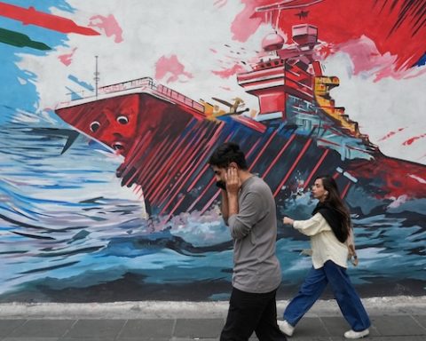 People walk past a mural depicting a U.S. aircraft carrier under missile attack in downtown Tehran, Iran, Sunday, May 17, 2026. (AP Photo/Vahid Salemi)