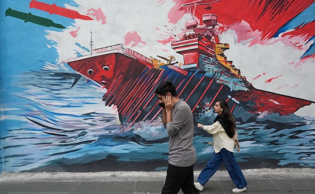 People walk past a mural depicting a U.S. aircraft carrier under missile attack in downtown Tehran, Iran, Sunday, May 17, 2026. (AP Photo/Vahid Salemi)