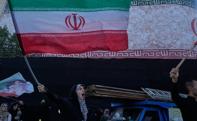 A woman waves an Iranian flags as she chants slogans against Iran and U.S. talks at the Islamic Revolution square in Tehran, Iran, Sunday, June 14, 2026. (AP Photo/Vahid Salemi)