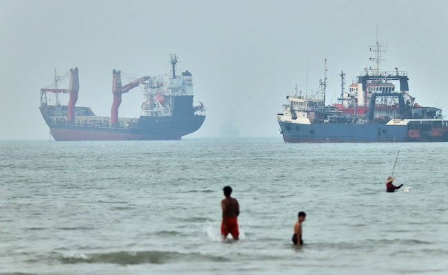 Children wade in the water with cargo ships at anchor in the background and a fisherman nearby, in the Strait of Hormuz off Bandar Abbas, Iran, Tuesday, June 30, 2026. (Amirhosein Khorgooi/ISNA via AP,File)